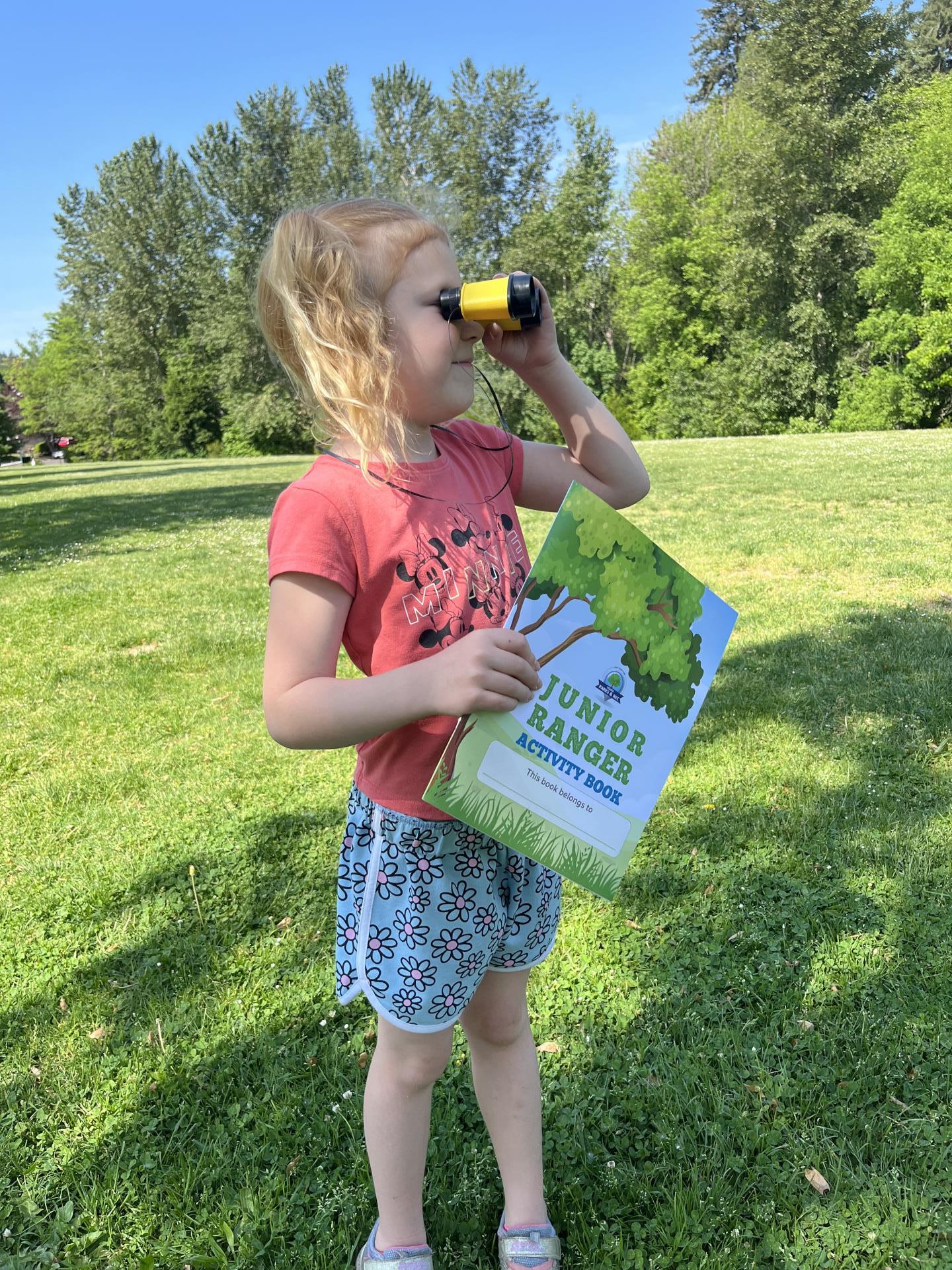 Image of child looking through binoculars holding the junior ranger activity book