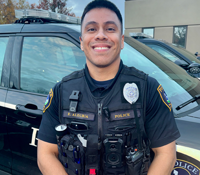 A close-up of a police uniform shoulder patch. The patch is blue with yellow trim and lettering, reading 'POLICE TIGARD OR,' and features a graphic of buildings and greenery.